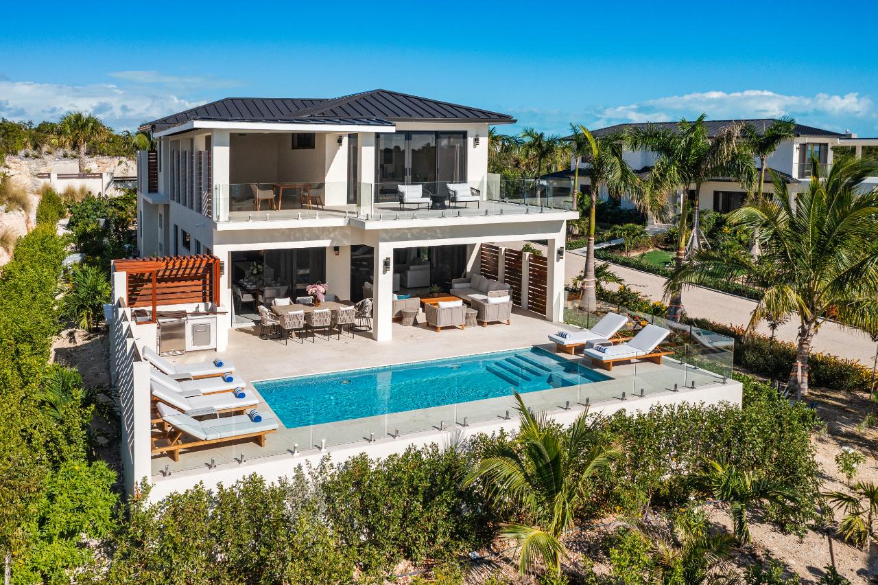 A beachfront villa in Turks and Caicos with white sand in the foreground and turquoise water beyond the patio