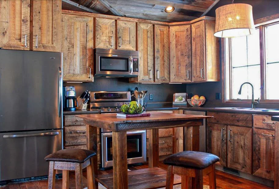 A bright kitchen with reclaimed wood cabinet fronts, a stone island, and large windows letting in natural light