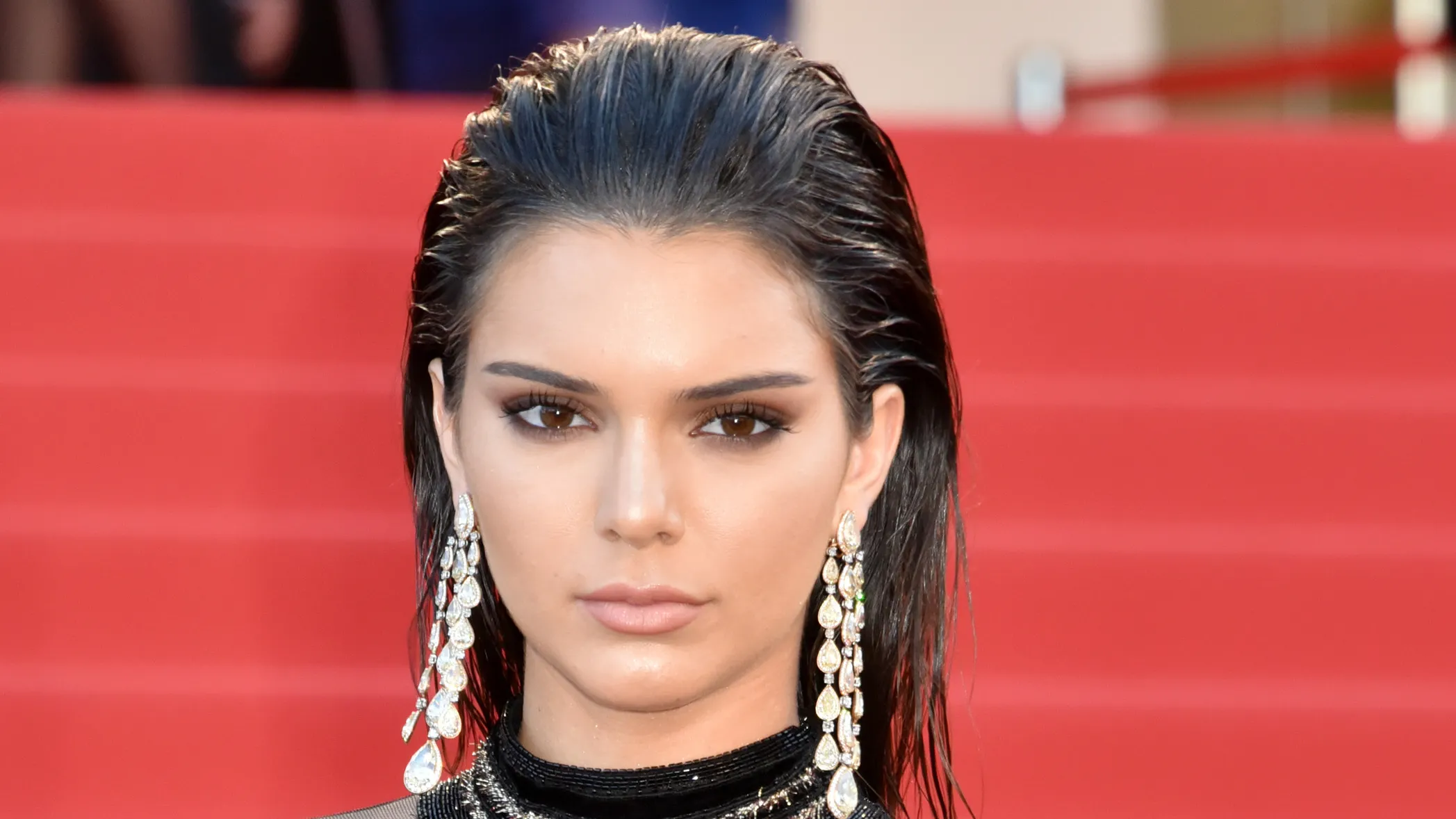 A celebrity arriving at a red carpet event with hair styled in a slicked-back wet-look, high shine at the roots and controlled texture through the lengths