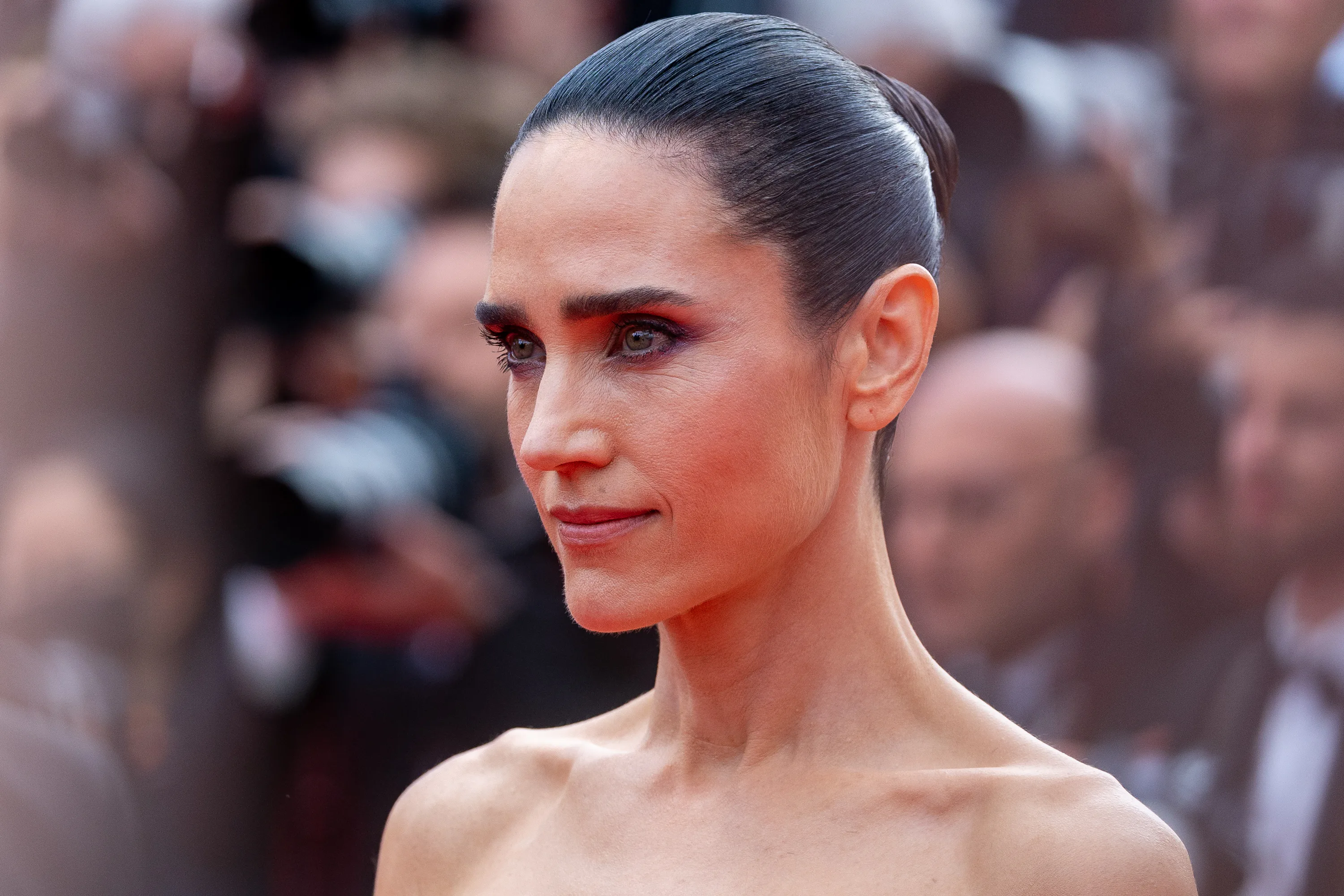 A celebrity on a red carpet wearing a minimalist gown with a sleek, center-parted low bun and a glossy, smooth hairline