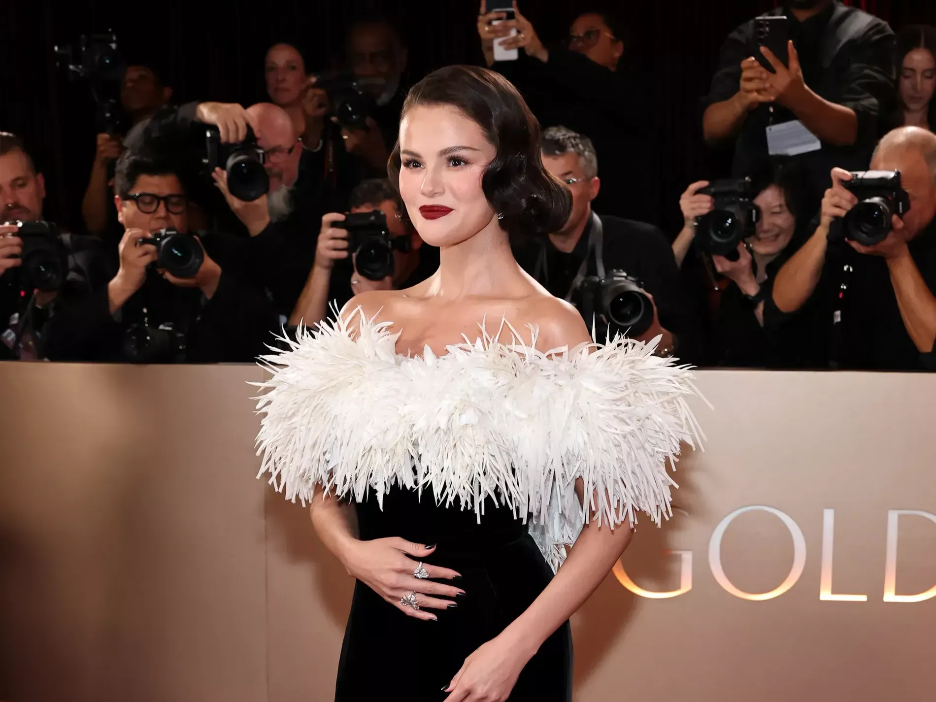 A celebrity on an awards show red carpet wearing a strapless gown with polished, brushed-out Hollywood waves and a deep side part