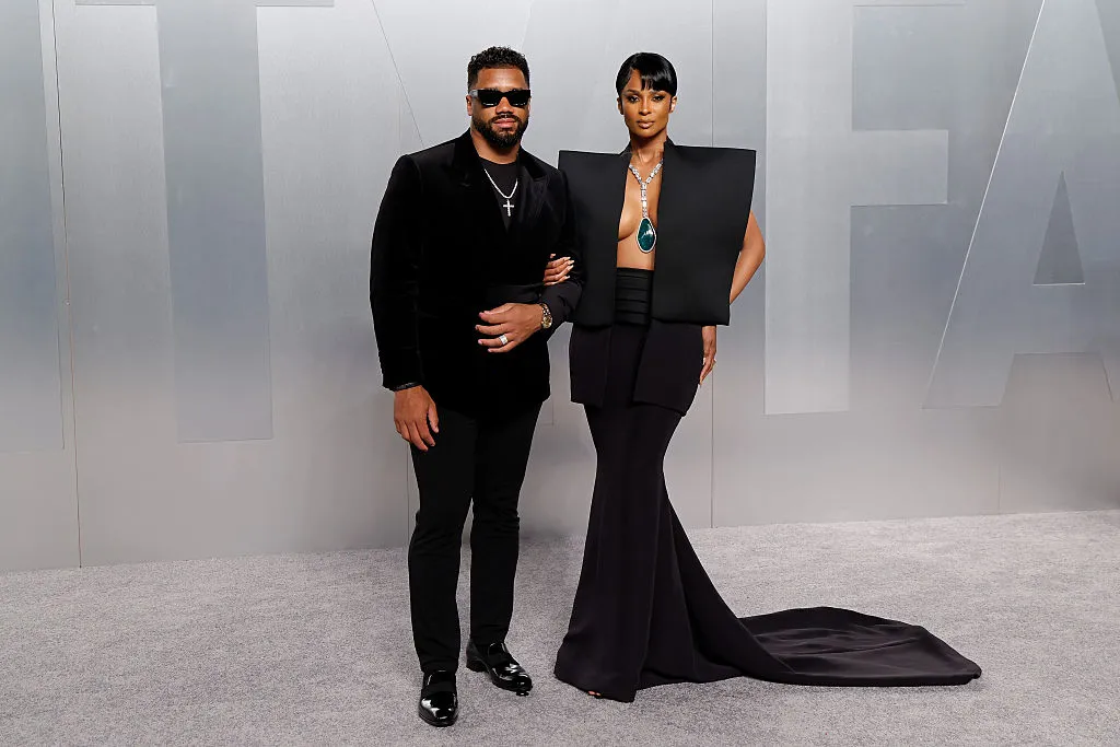 A celebrity steps out of a black SUV outside an Oscars after-party venue at night while a stylist lifts the hem of a second outfit.