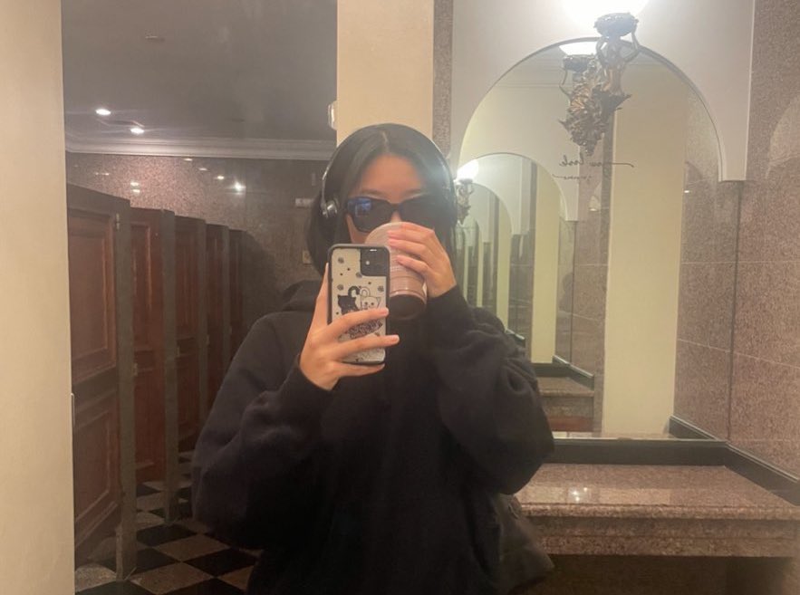 A celebrity taking a mirror selfie in a modern bathroom with a straight mirror edge, a countertop, and a visible faucet