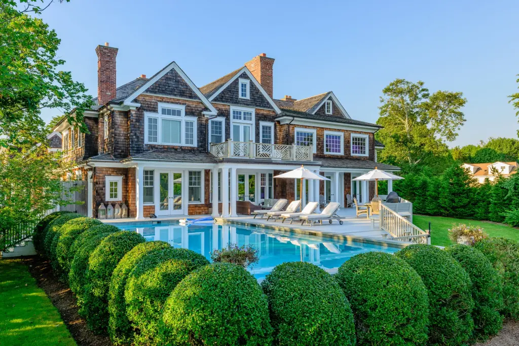 A classic shingle-style Hamptons home with hydrangeas in bloom and a wide porch in soft golden-hour light