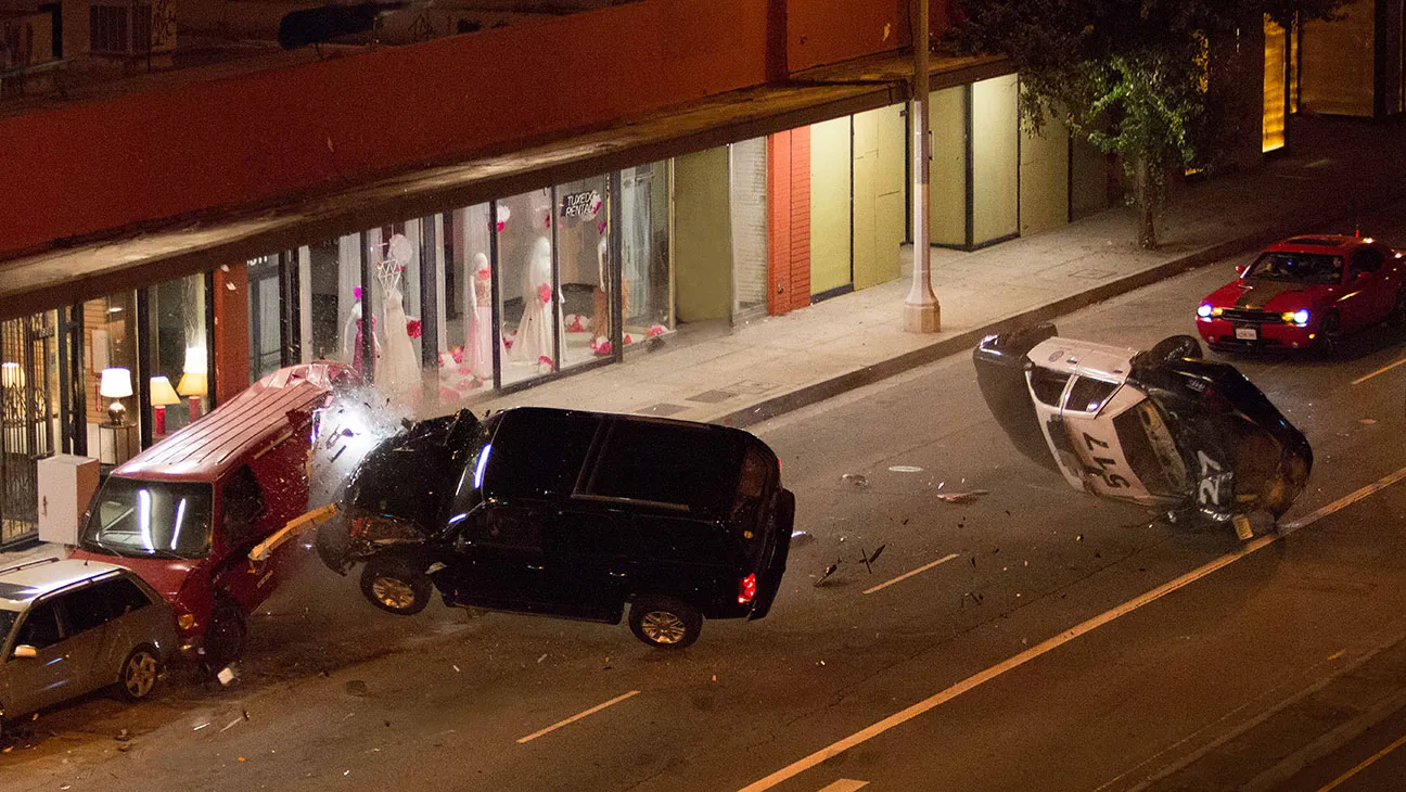 A cluster of photographers gathered near cars on a Los Angeles street at night, aiming cameras toward a vehicle