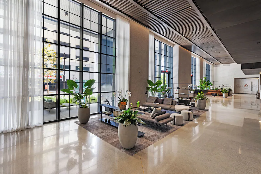 A daytime photograph of a high-end condo tower lobby with a doorman desk, an elegant seating area, and tall glass entry doors