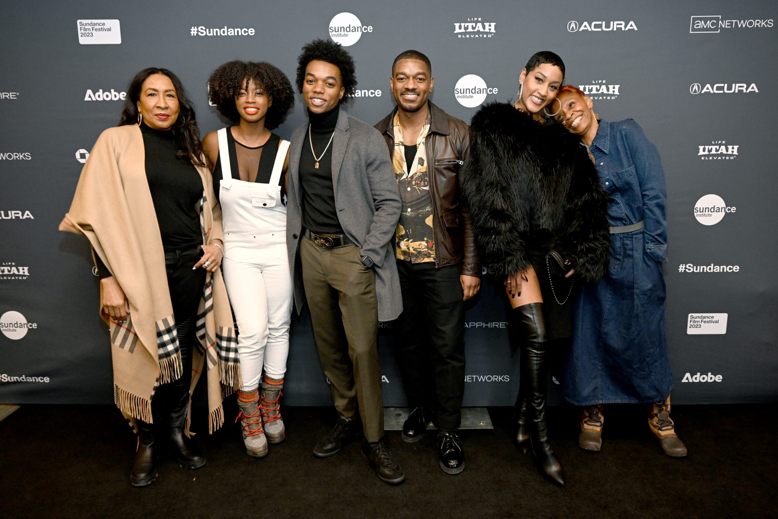 A filmmaker and cast posing onstage at a Sundance Film Festival premiere event with theater lighting and an audience visible.