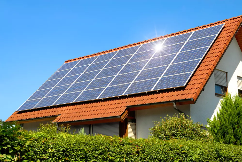 A home with rooftop solar panels generating electricity in bright sunlight, with clean rooflines and a well-kept yard
