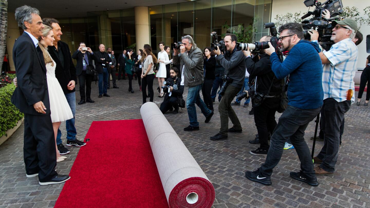 A line of photographers with cameras raised behind a barricade at a Los Angeles red carpet event at night, with bright flashes going off
