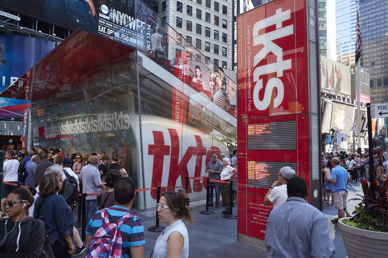 A line of theatergoers waiting at a Broadway box office window during the daytime in New York City.
