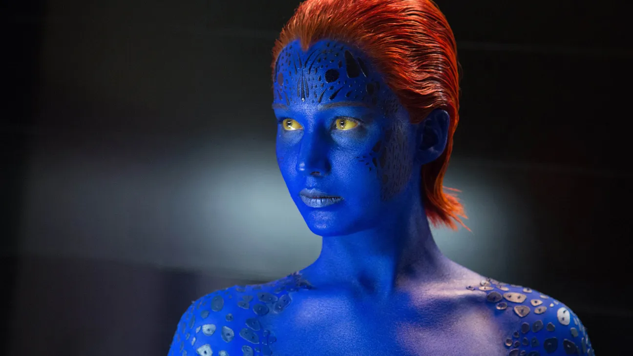 A live-action portrayal of Mystique with blue skin and distinctive facial texture, photographed in a dramatic, cinematic lighting setup