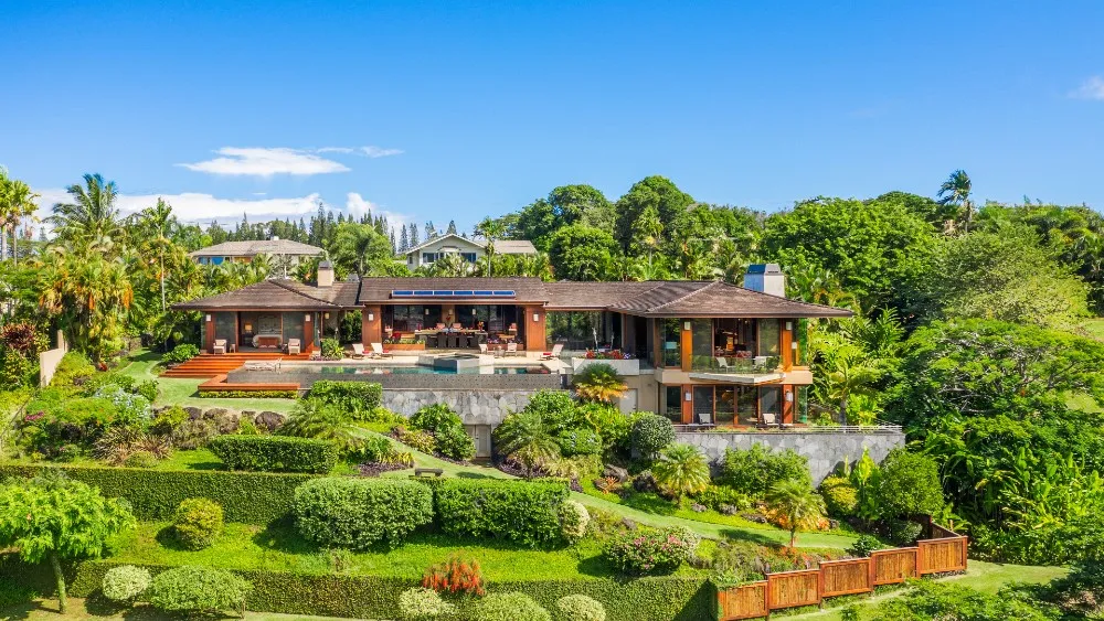 A luxury home on Kauai with a shaded lanai, lush tropical plants, and an ocean view under soft afternoon light