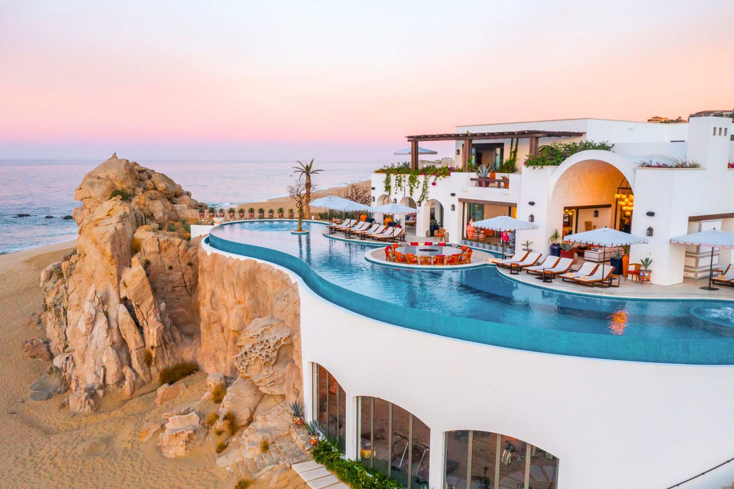 A luxury villa in Los Cabos with an infinity pool facing the ocean, modern outdoor seating, and warm sunset light