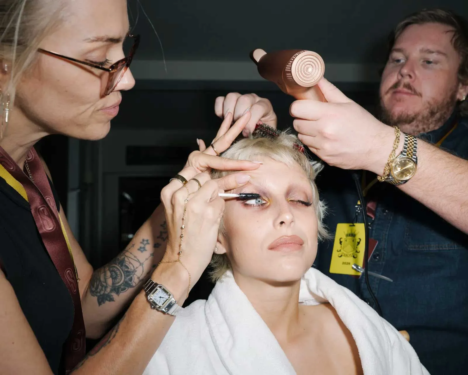 A makeup artist in a backstage dressing area applying translucent powder with a velour puff to a celebrity's under-eye area