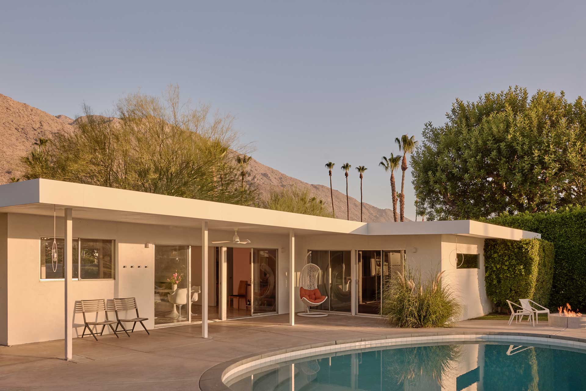 A midcentury modern Palm Springs home with a rectangular pool, desert landscaping, and mountains in the background under a clear sky