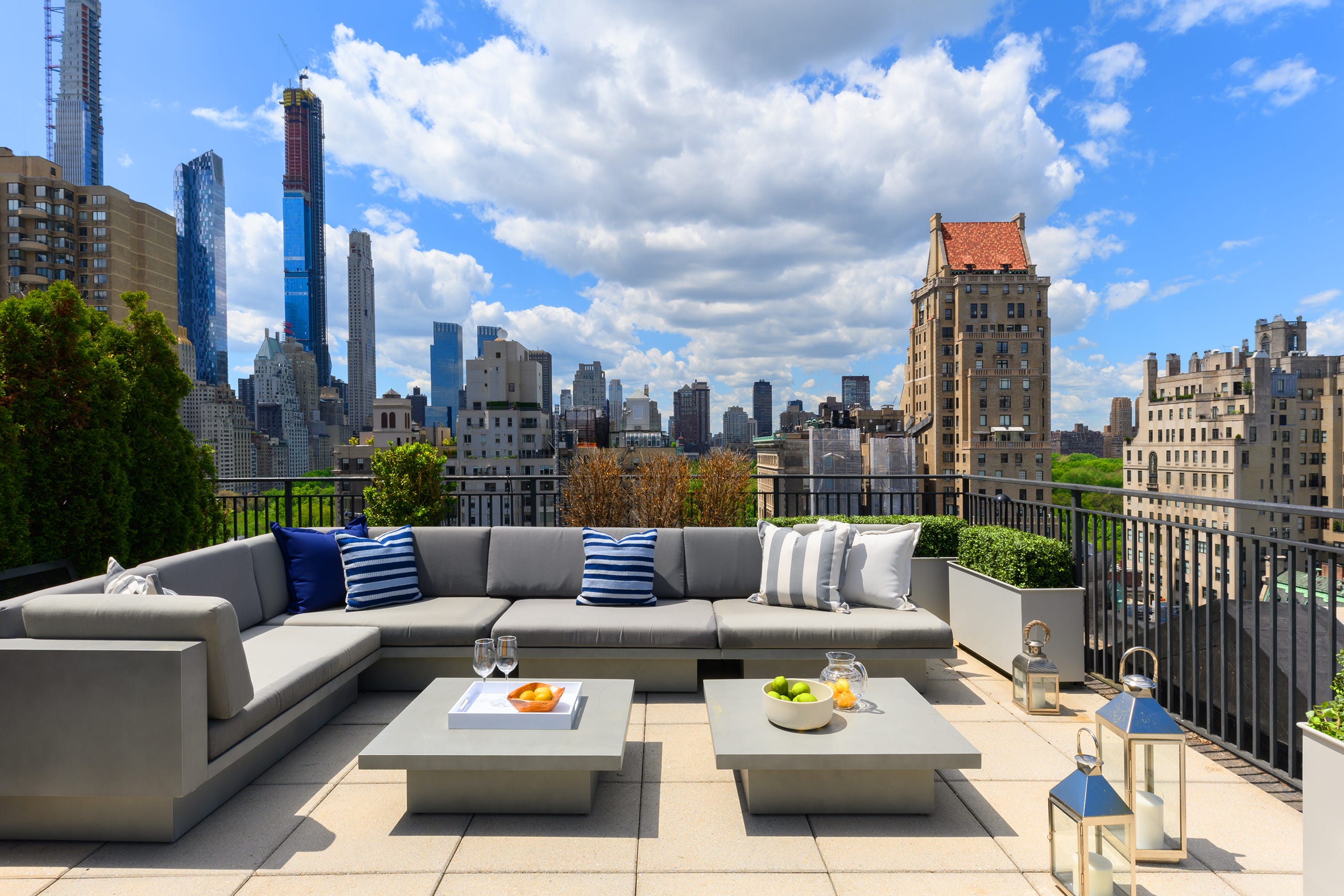 A nighttime photograph of a luxury penthouse terrace overlooking the Manhattan skyline, with outdoor lounge seating and warm ambient lighting