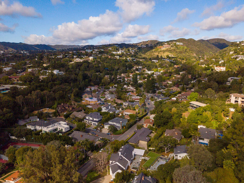 A quiet residential street in Brentwood, Los Angeles, lined with trees and upscale homes in the background