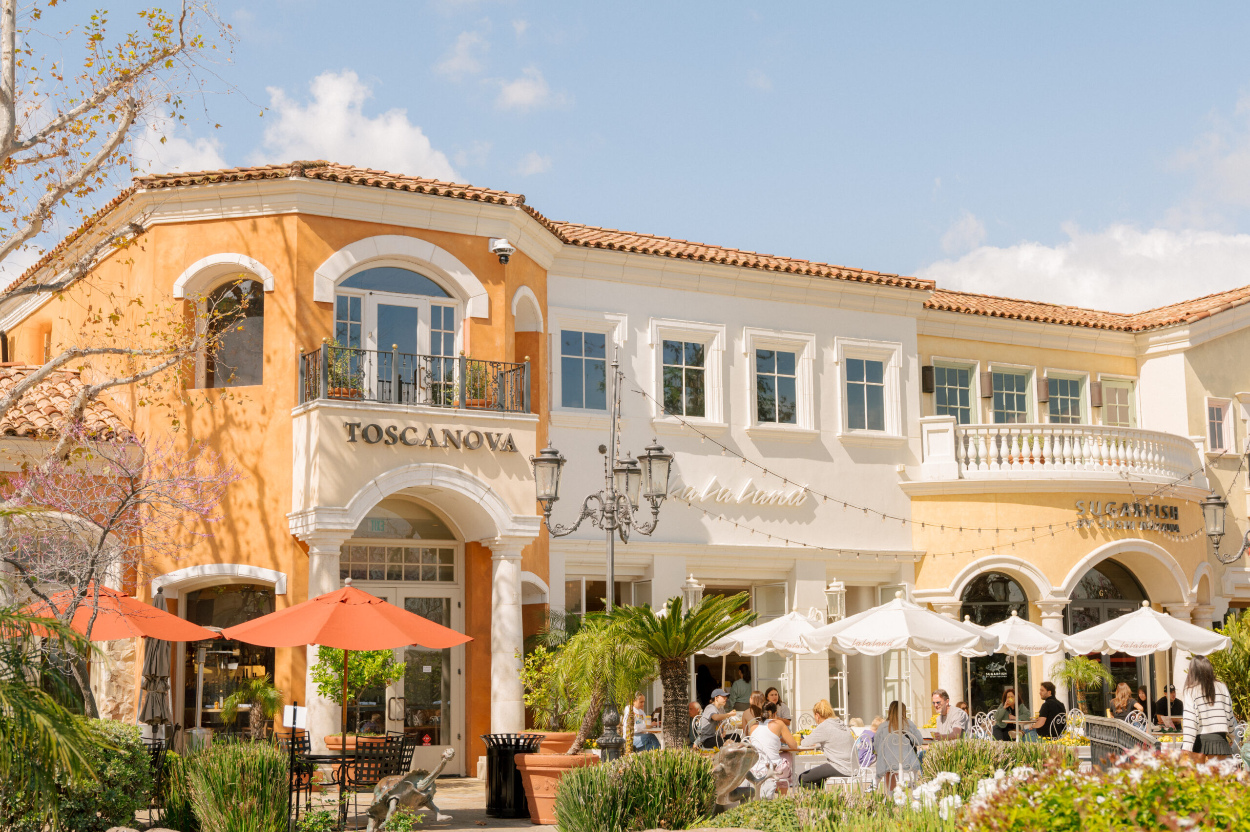 A real photograph of The Commons at Calabasas outdoor shopping center with storefronts, patio seating, and palm trees in warm daylight