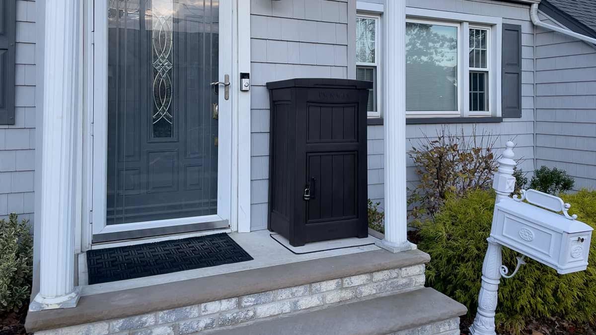 A secure locked parcel delivery box placed on a front porch near a door, designed to keep packages out of sight