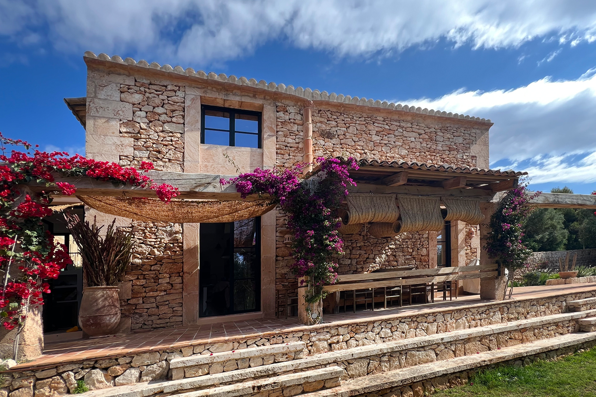 A traditional Mallorca finca with stone walls, a swimming pool, and olive trees under bright Mediterranean sunshine