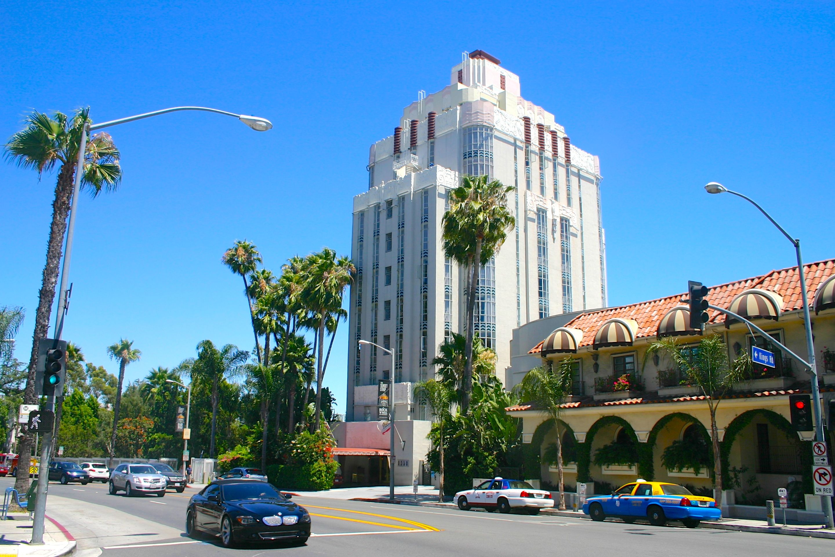 A twilight photograph of traffic along Sunset Boulevard in West Hollywood with palm trees and glowing storefront signs