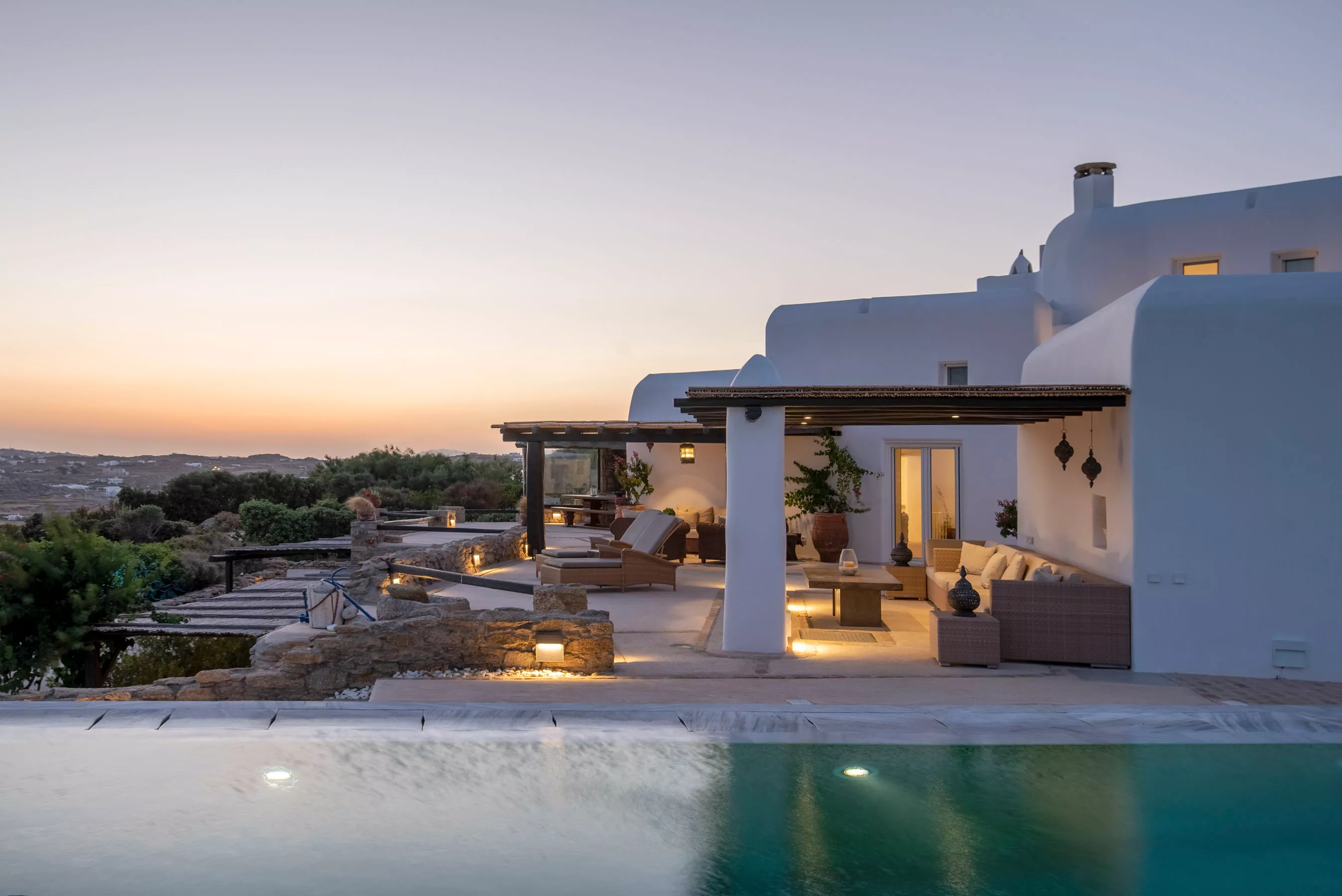 A whitewashed Mykonos villa with an infinity pool overlooking the Aegean Sea during a vivid sunset