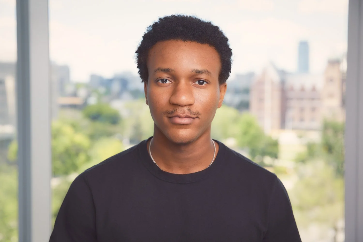 A young actor standing near a window in natural light for a clean, simple headshot photo with a neutral background