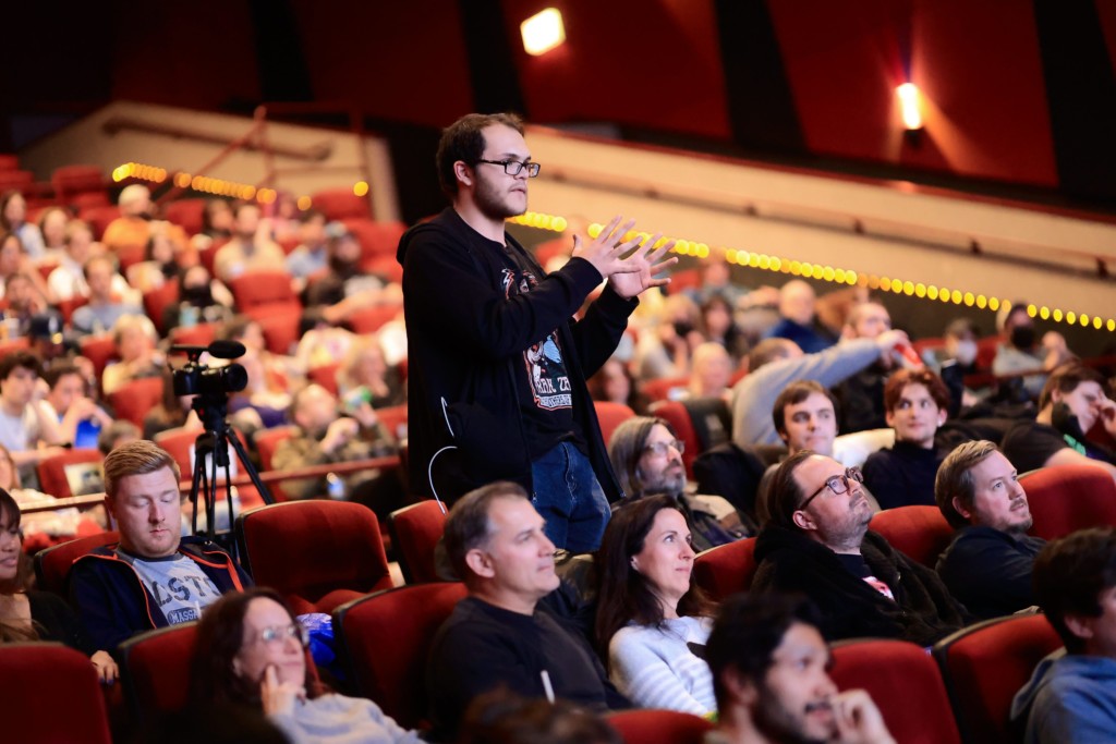 An audience seated in a small theater listening to a filmmaker speaking into a microphone during a post-screening Q&A