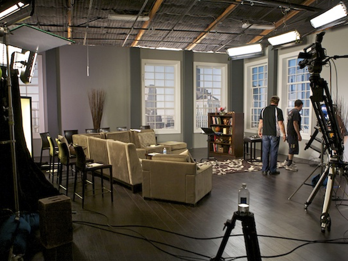 Background actors seated quietly in a studio holding area with folding chairs and craft service tables, waiting for their next call