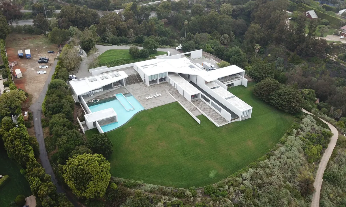 Beyoncé and Jay-Z arriving near a secluded coastal luxury property in Malibu with ocean views and tall privacy hedges, photographed from a respectful distance