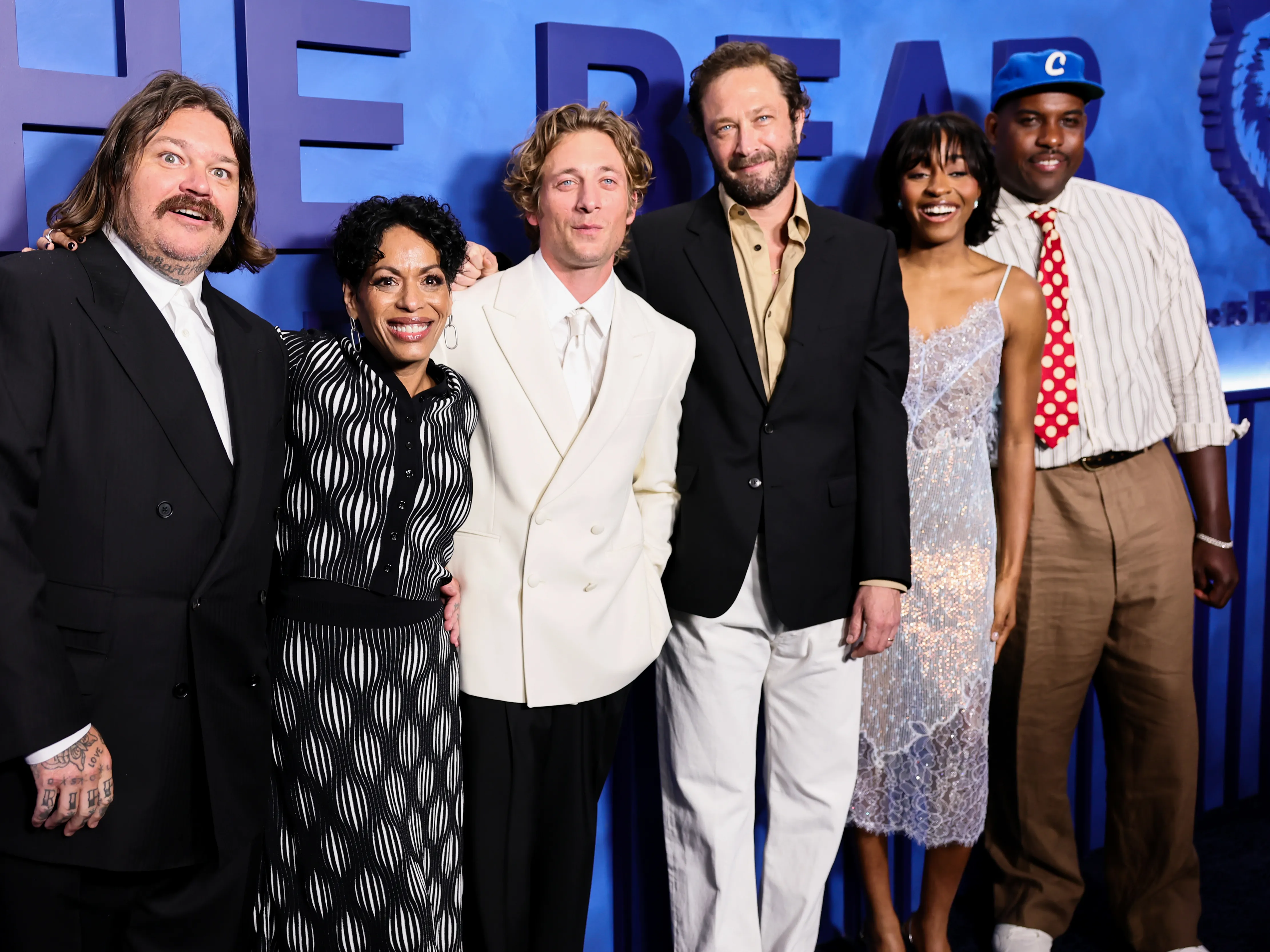 Cast members from FX's The Bear posing together at an industry event, wearing modern formal outfits and smiling for photographers