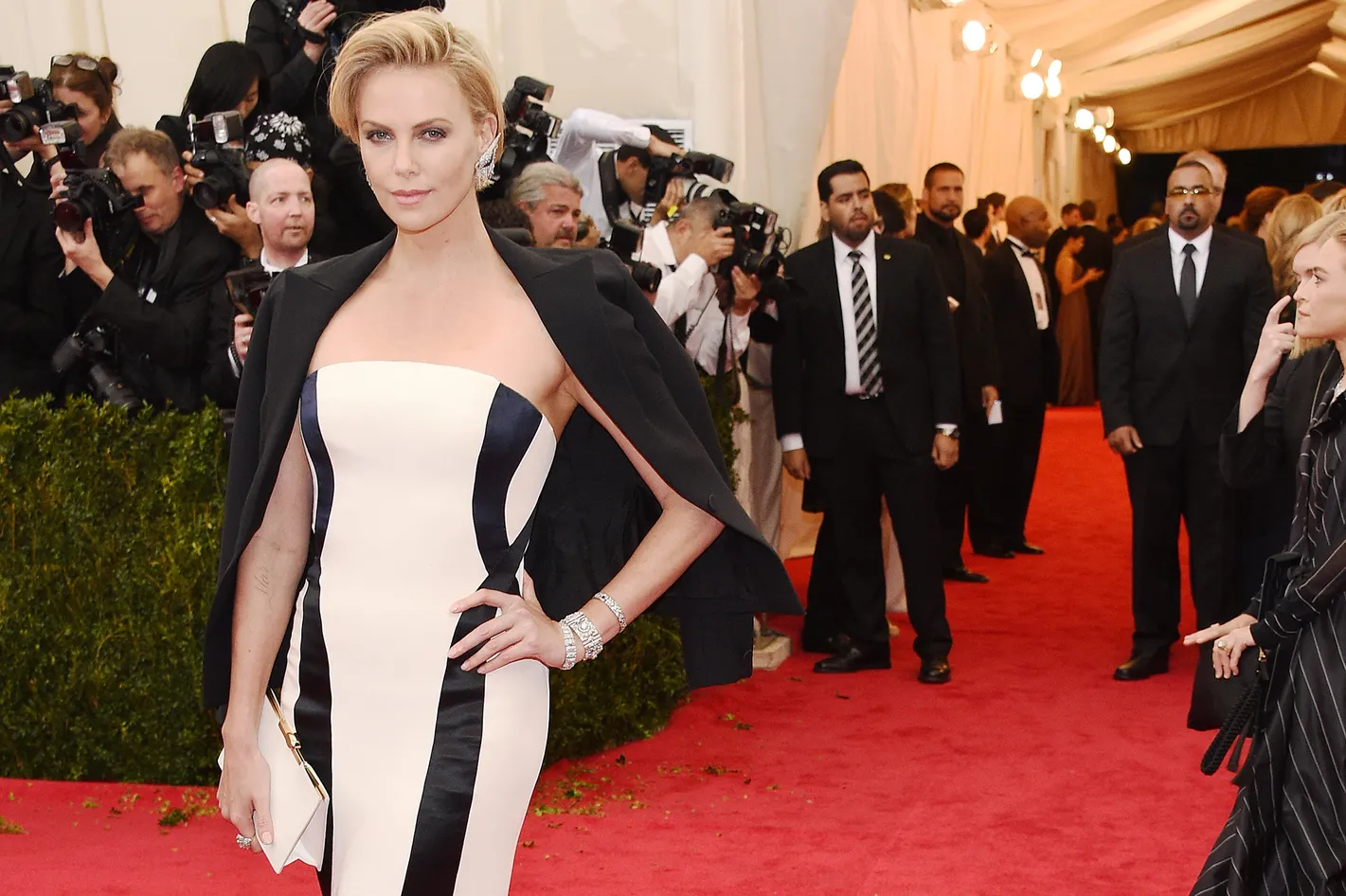 Charlize Theron posing on a red carpet in a sleek bodice paired with a gown silhouette that flares subtly below the hips, creating balanced proportions under bright event lighting