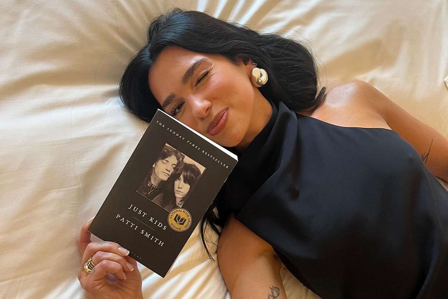 Dua Lipa holding a book while looking toward an audience at an event.