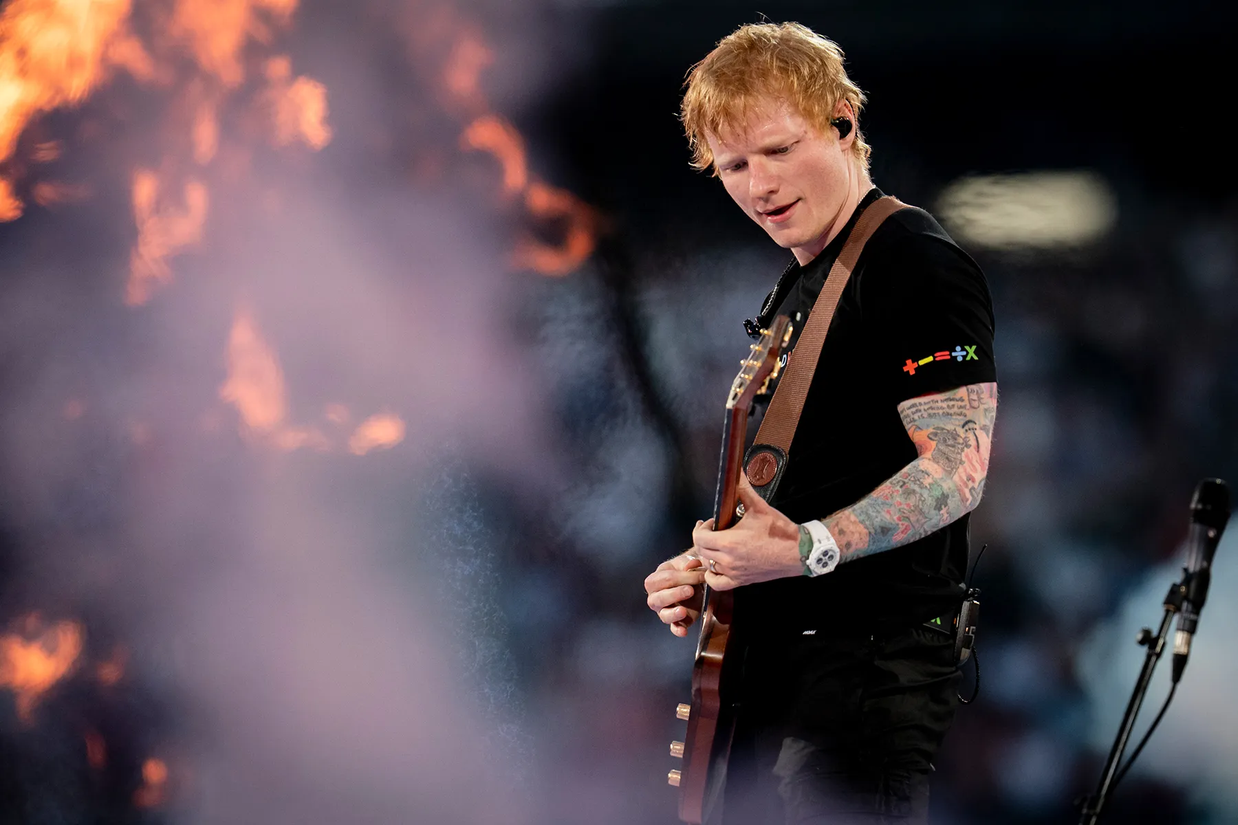 Ed Sheeran performing onstage during a tour show while holding a guitar