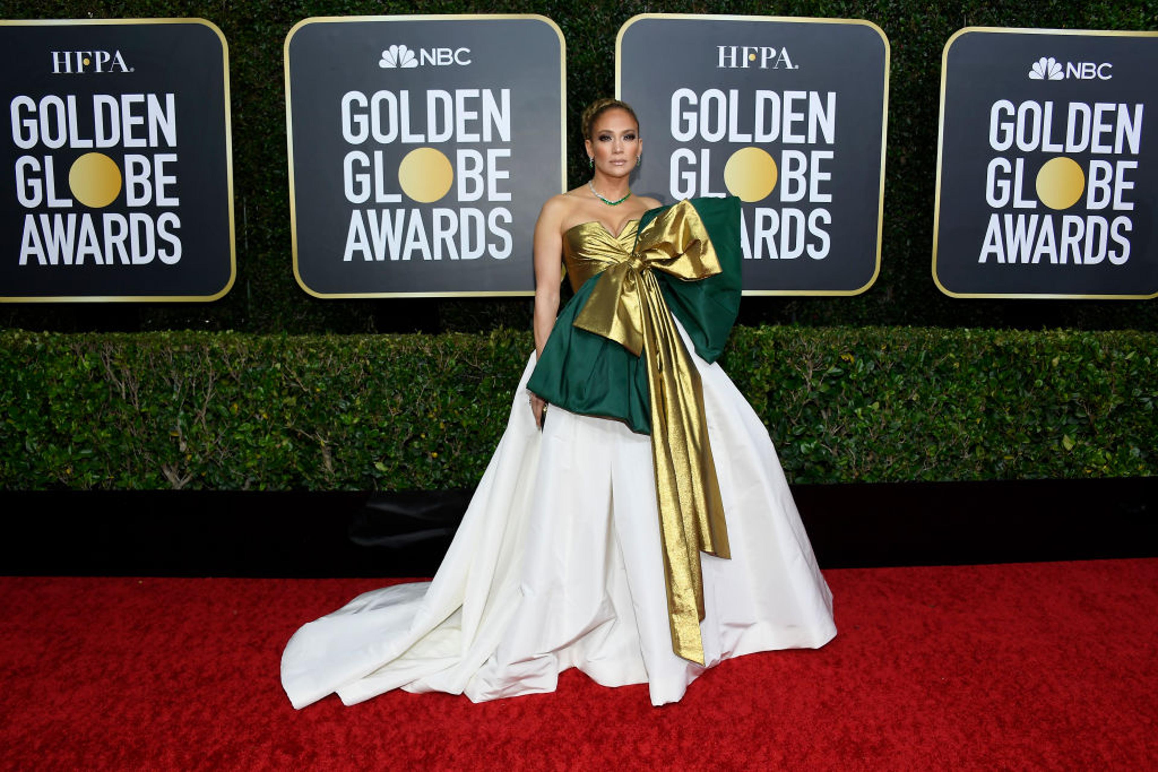 Jennifer Lopez on a red carpet wearing a glamorous gown with a defined waist and a fuller skirt, her shoulders emphasized by a bold neckline, photographers in the background