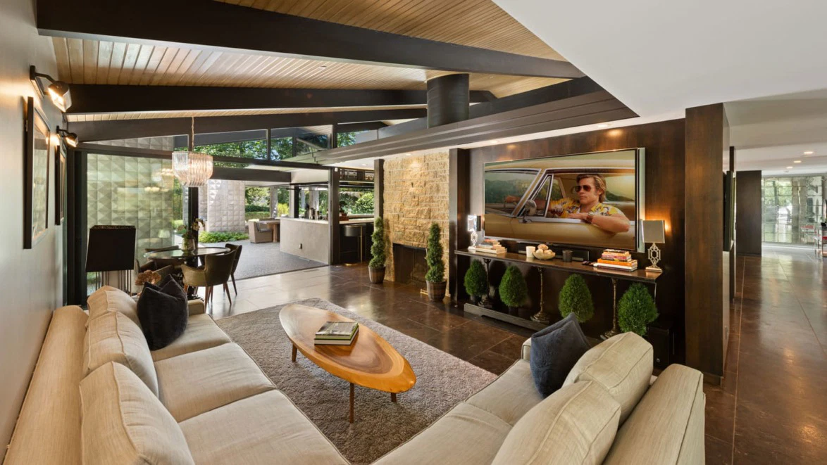 Jeremy Renner standing outside a renovated home with fresh exterior paint, updated landscaping, and a clean, modern entry