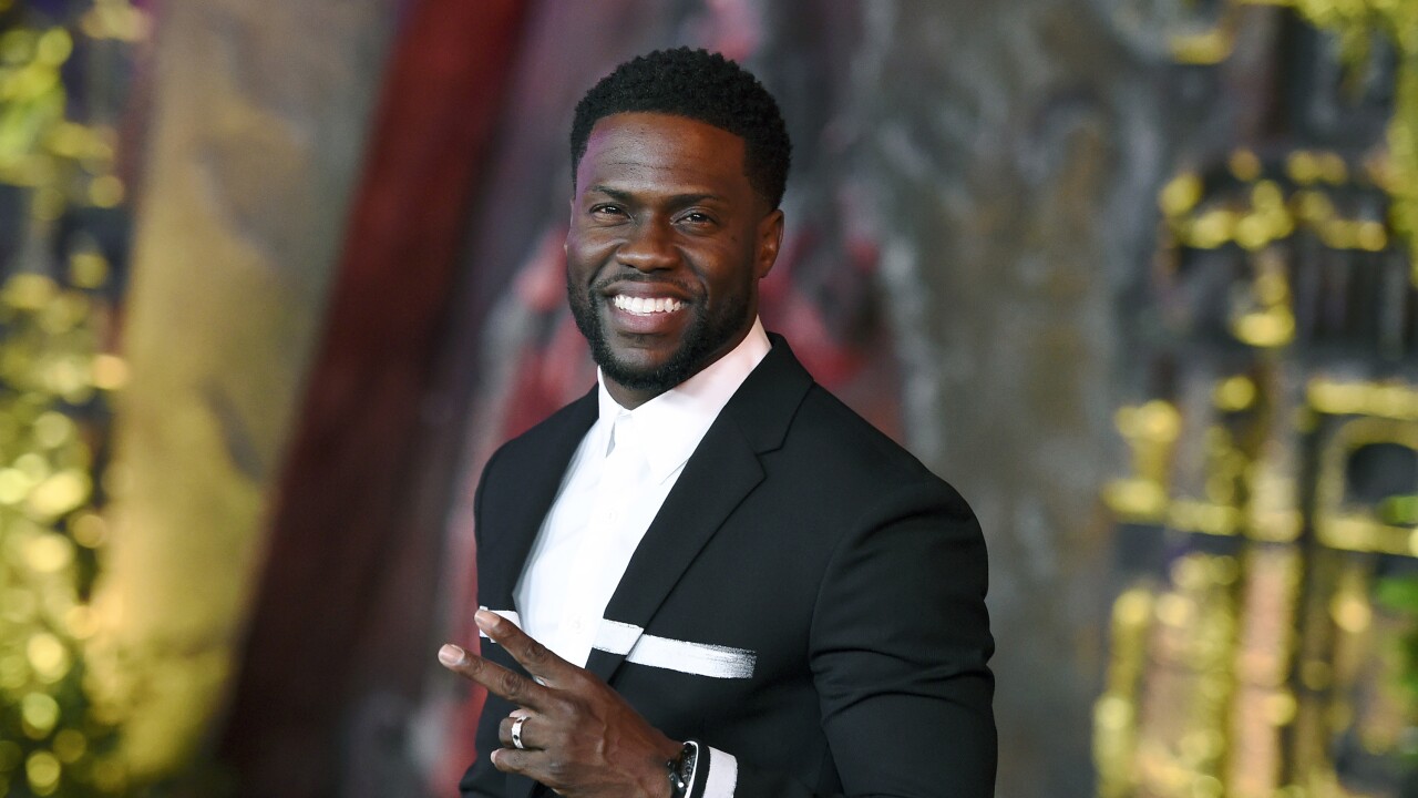 Kevin Hart arriving at a charity event in a tailored suit, photographed on a step-and-repeat with event lighting
