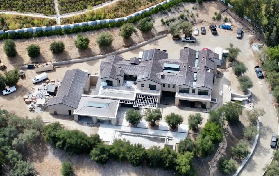 Kylie Jenner walking up a modern driveway toward a gated Hidden Hills estate with minimalist architecture and a landscaped entry