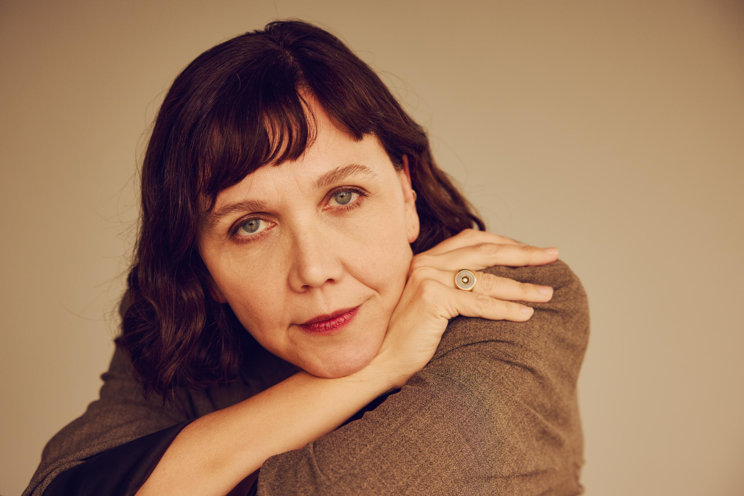 Maggie Gyllenhaal at a film event, speaking to press while standing in front of a step-and-repeat backdrop