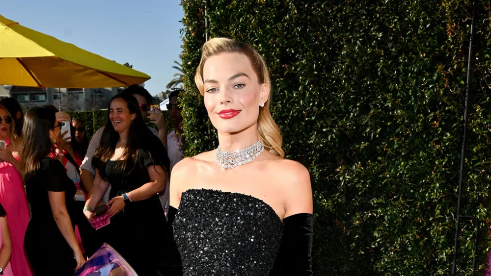Margot Robbie arriving at a Barbie film premiere with bright flash photography and a crowded backdrop of fans and press