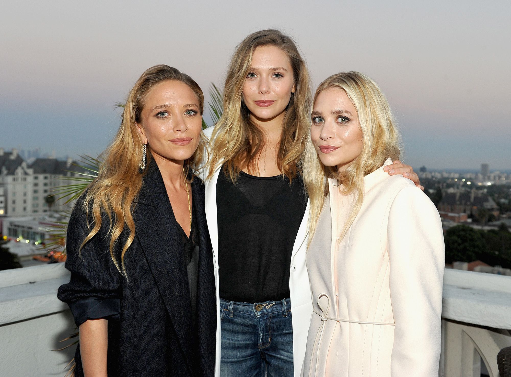 Mary-Kate Olsen, Ashley Olsen, and Elizabeth Olsen attending a public event together, standing close and smiling as photographers capture the moment