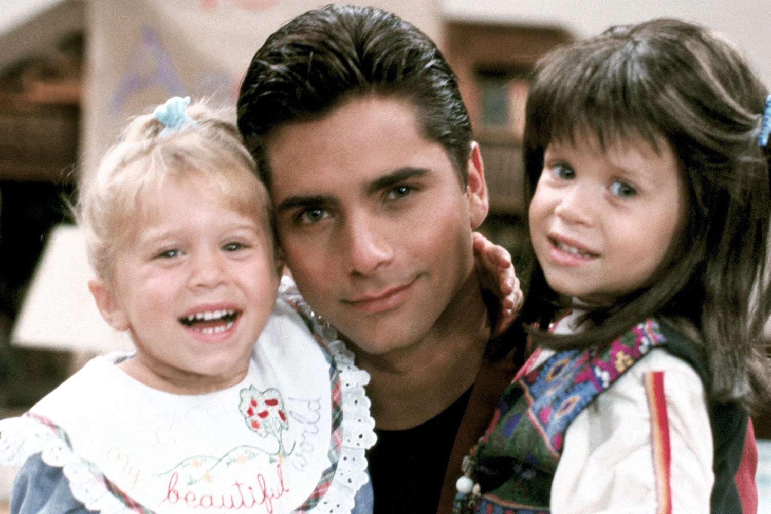 Mary-Kate Olsen and Ashley Olsen as toddlers on the set of Full House, standing in a cozy living room set with warm sitcom lighting
