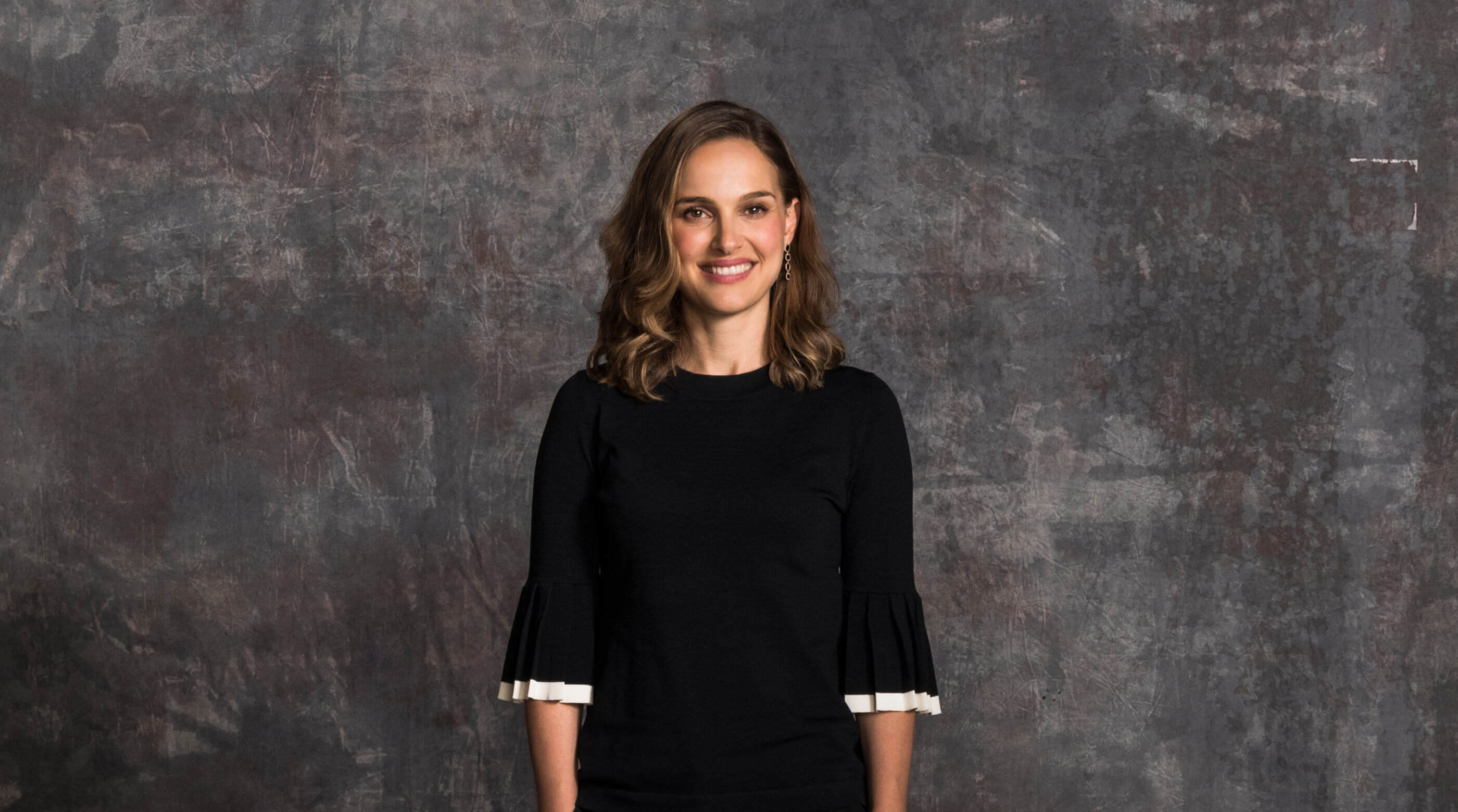 Natalie Portman seated in a studio interview setting, speaking thoughtfully to camera during a filmed lesson, cinematic lighting