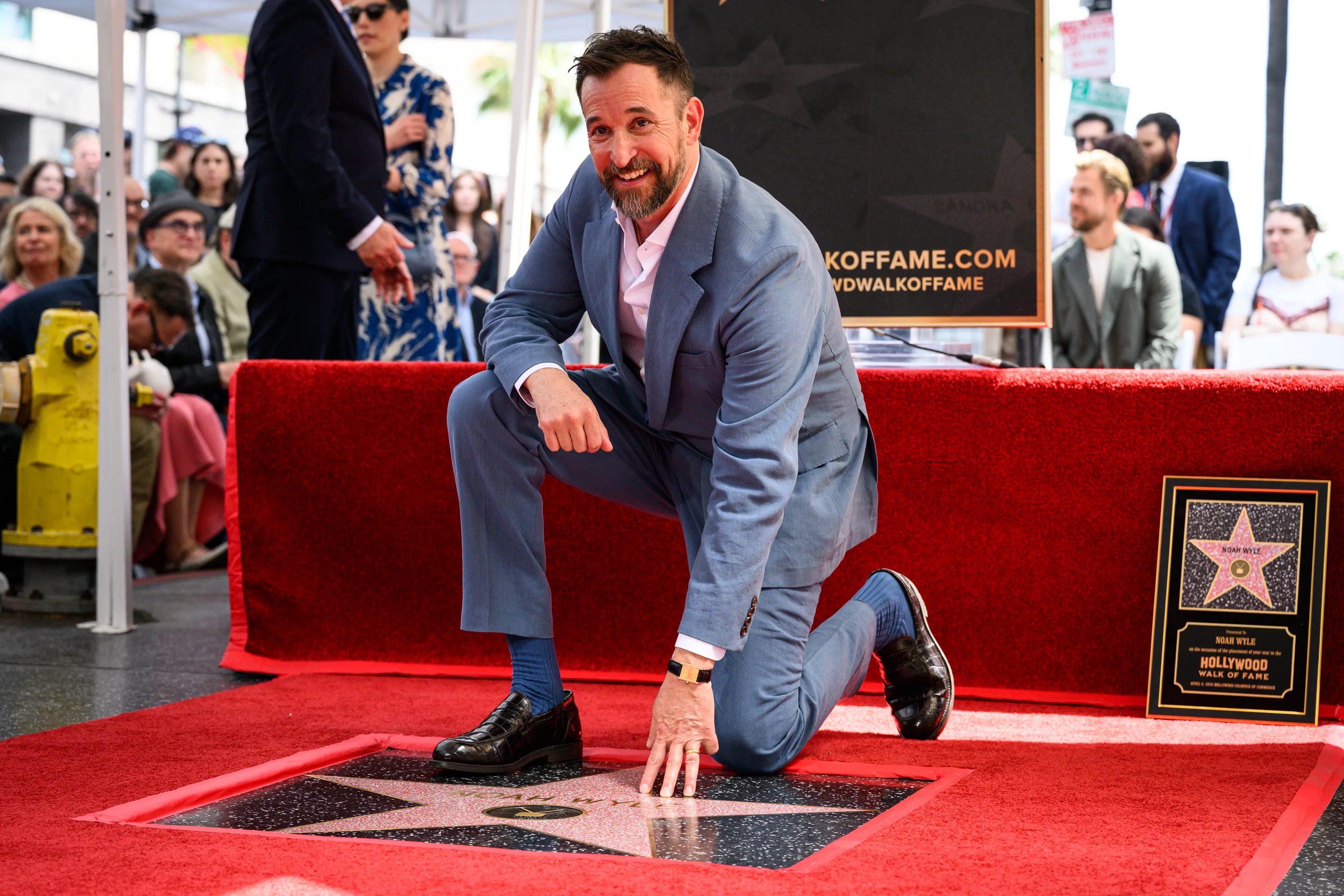 Noah Wyle at a public appearance, dressed in a tailored suit and posing for photographers