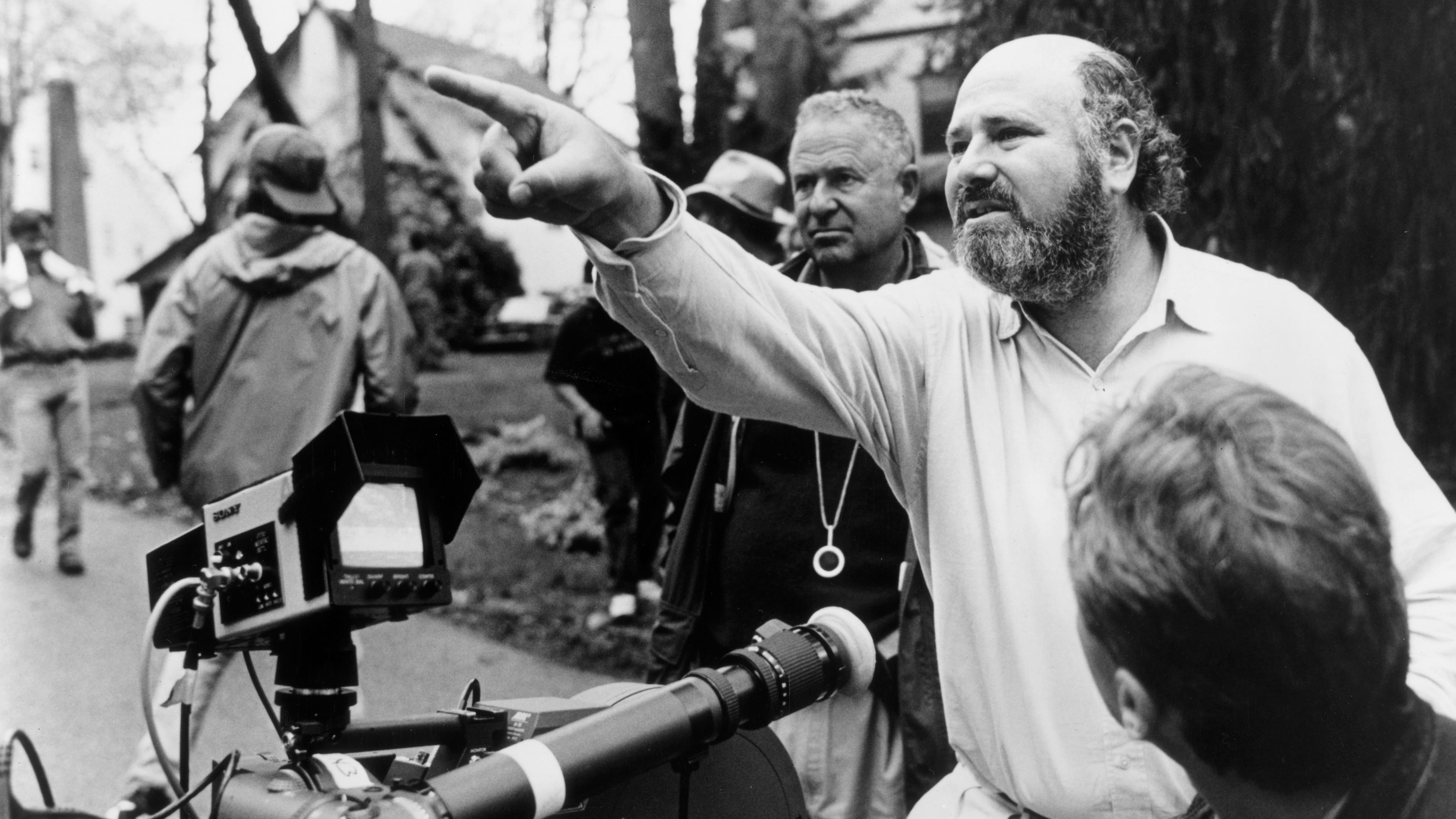 Rob Reiner on a film set wearing a headset, speaking with crew members near a camera rig