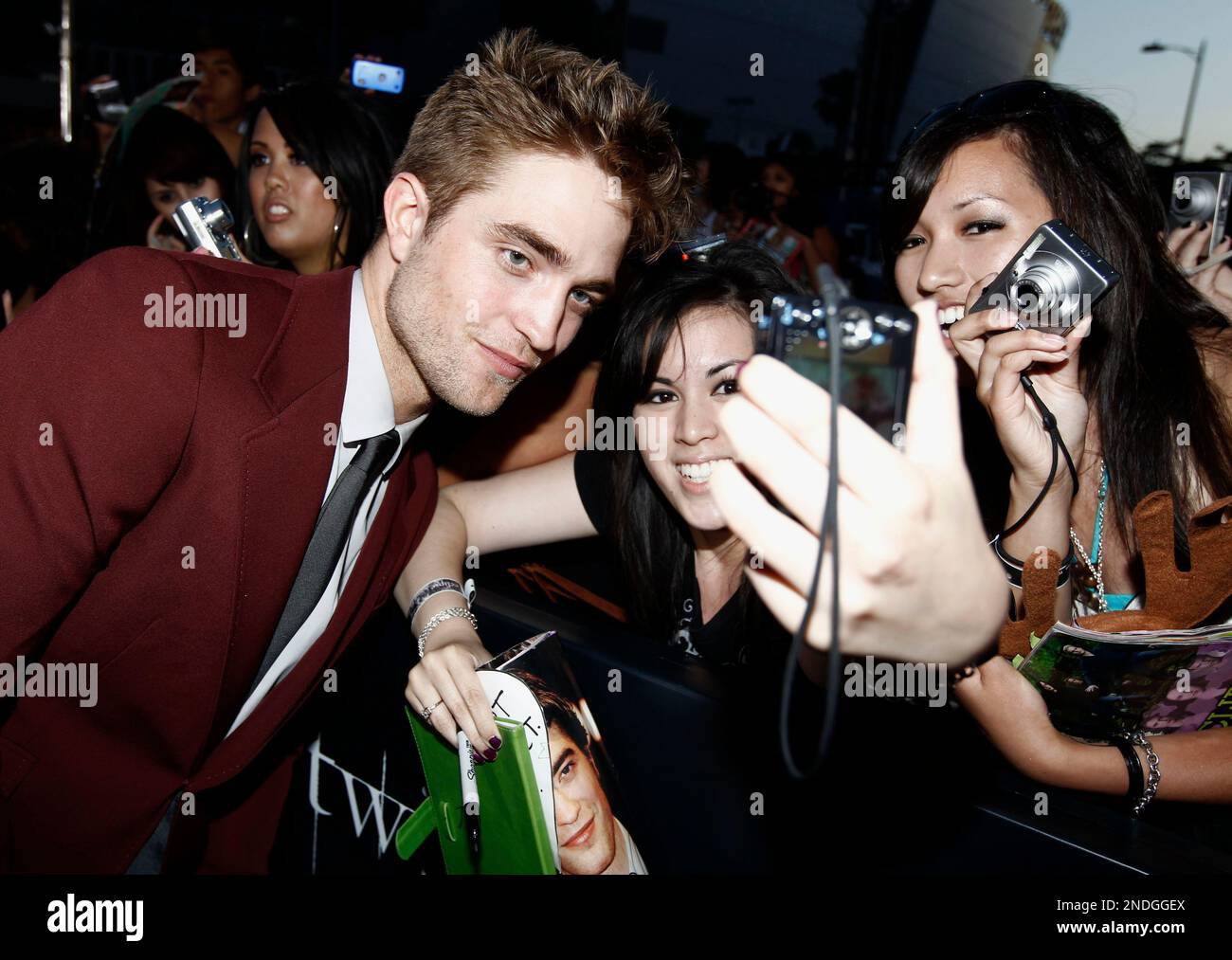 Robert Pattinson on a Twilight-era red carpet, wearing a dark suit and standing in front of fans and photographers