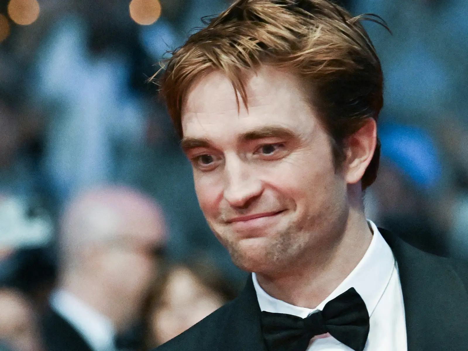 Robert Pattinson on a Twilight-era red carpet, wearing a dark suit and standing in front of fans and photographers