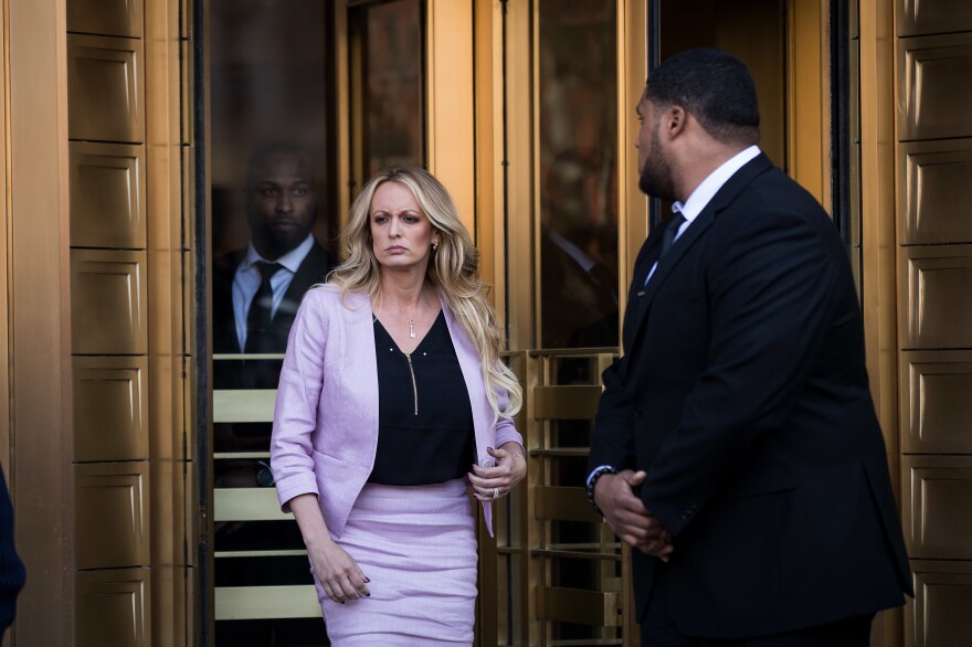 Stormy Daniels outside a courthouse walking with her attorney as reporters and cameras surround them