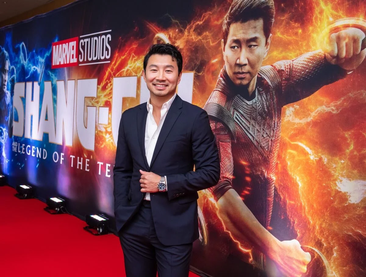 The actor who plays Shang-Chi attending a 2026 film premiere in a tailored suit, photographed on a red carpet under event lighting
