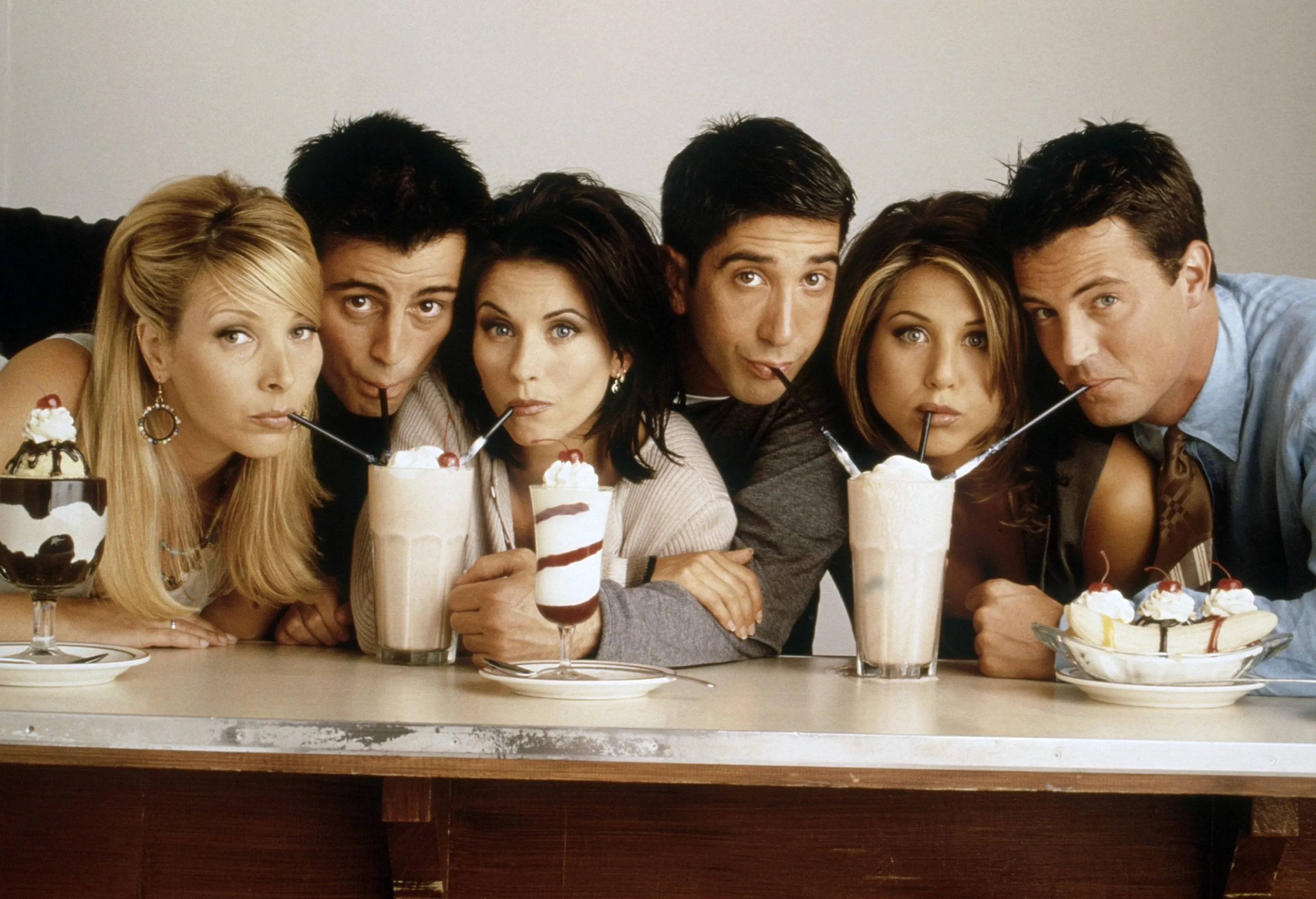 The main cast of the TV show Friends posing together at a 1990s promotional event, smiling for photographers
